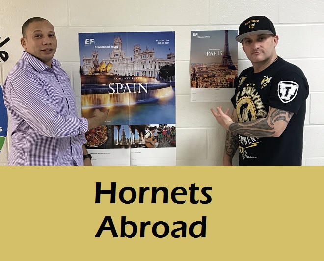 Mr Patterson and Mr Brewer point to a poster with the text Hornets Abroad